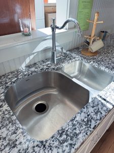 Close-up of stainless steel sink and faucet in Newport White Kitchen Cabinet Display with Gran Perla Granite countertop