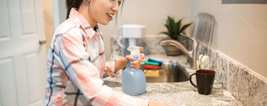 Person wiping down a kitchen countertop with a spray bottle and cloth